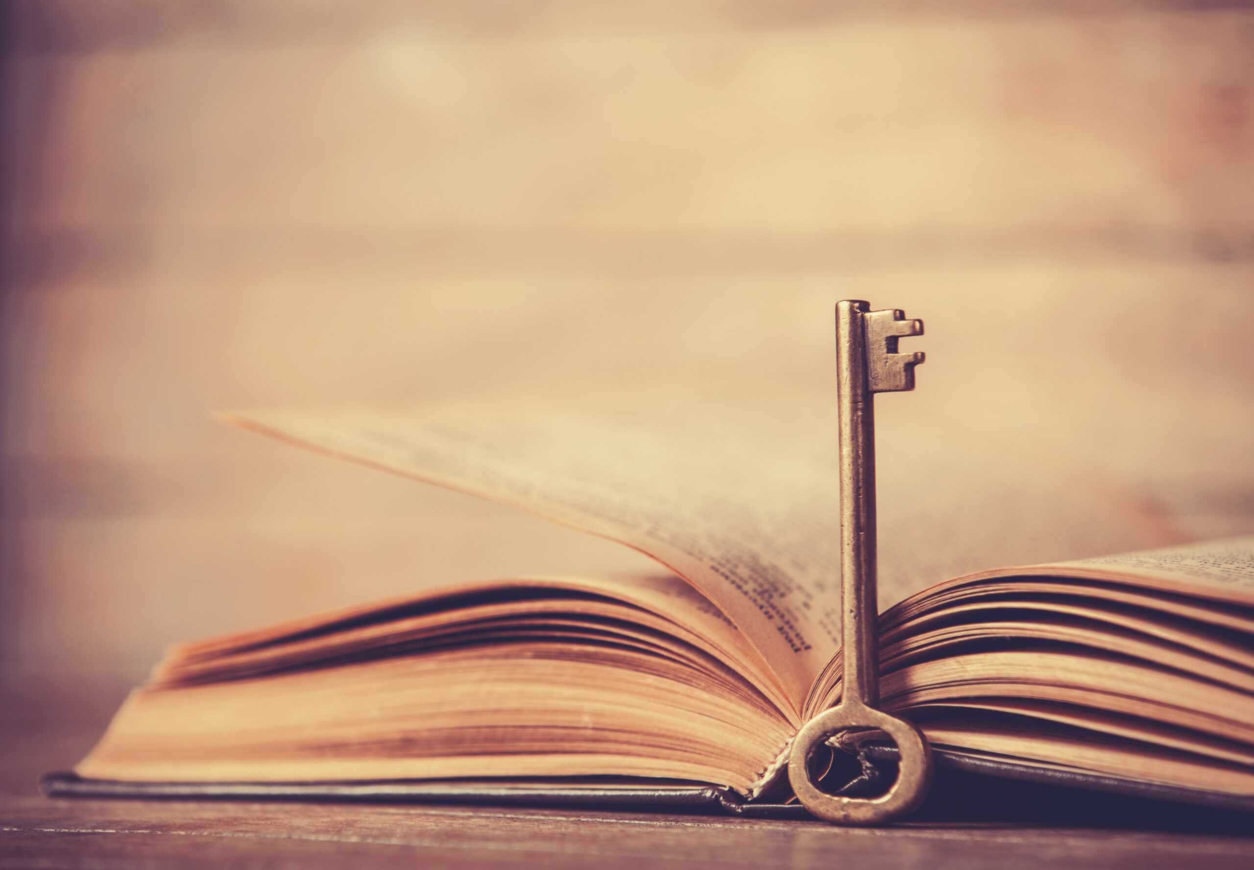 Retro key and opened book on wooden table.