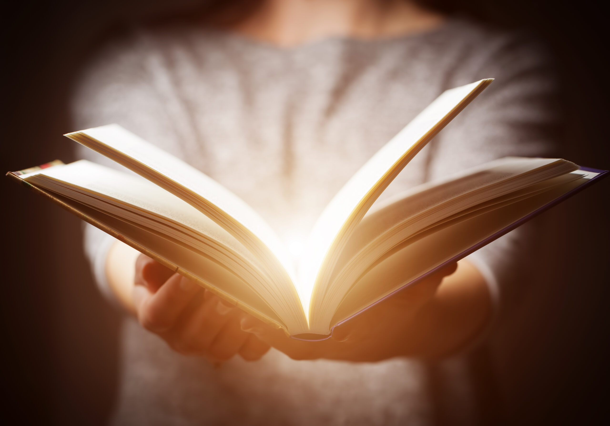 Light coming from book in woman's hands in gesture of giving, offering. Concept of wisdom, religion, reading, imagination.